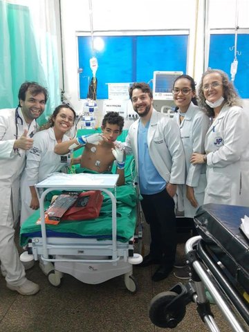 João Victor recebendo as luvas de presente do Dr. Vinicius Ortigosa, com parte da equipe da sala vermelha do JPII - Gente de Opinião