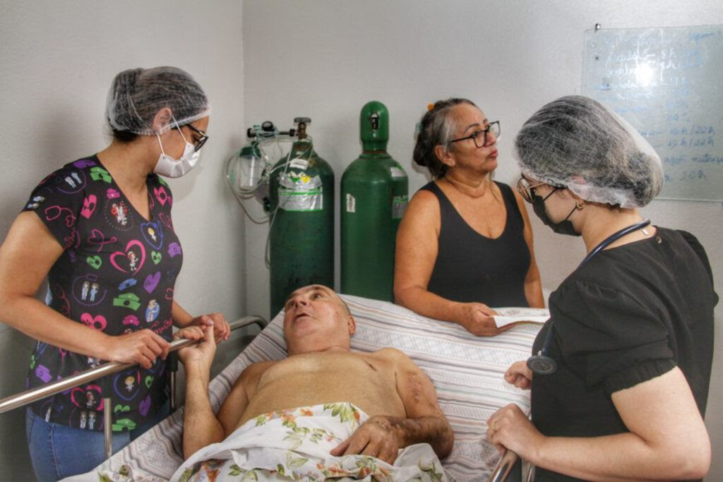 Na cabeceira da cama, a esposa e cuidadora Bernardina; à esquerda, a enfermeira Dayse, à direita, a médica Fernanda - Gente de Opinião